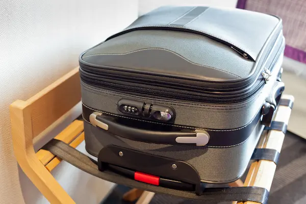 A suitcase stand with a gray suitcase on it in a hotel room.