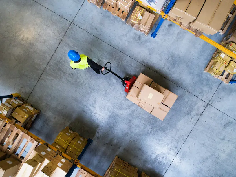 Warehouse worker pulling a hand truck loaded with product.